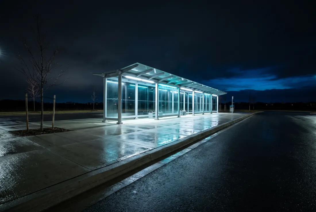Generated scene: an empty transit shelter with a long glass canopy glowing cyan at night, a wet platform and a dark sky.